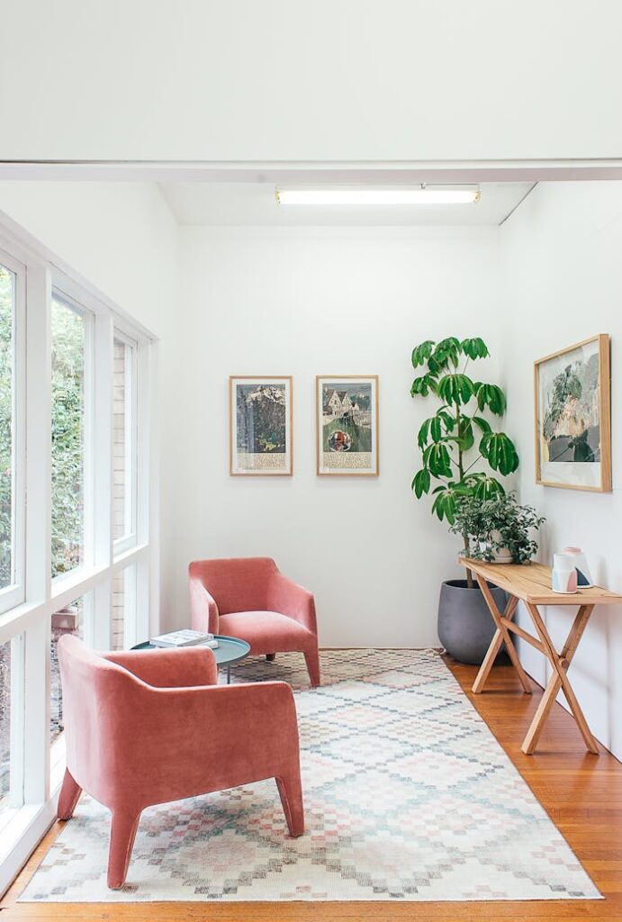 Bright, minimalist reading nook featuring pink armchairs, leafy plants, and modern artwork.